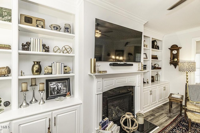 living area with built in features, ornamental molding, a ceiling fan, a high end fireplace, and dark wood-style floors