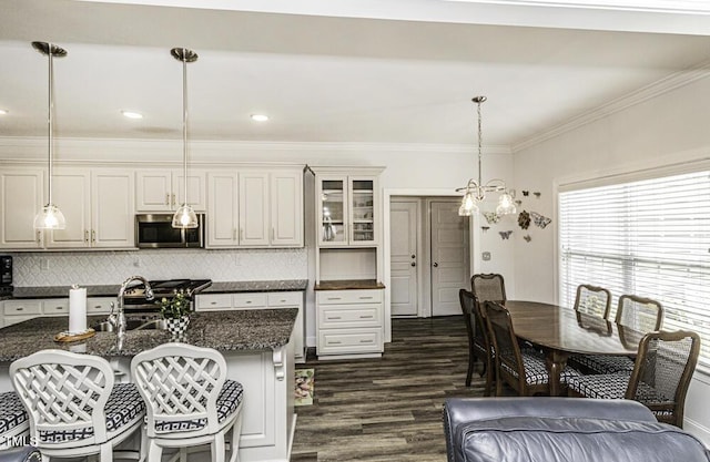 kitchen with crown molding, dark wood finished floors, stainless steel microwave, decorative light fixtures, and a breakfast bar area