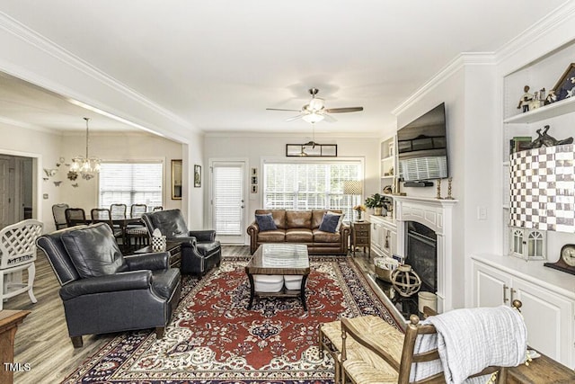 living room with crown molding, wood finished floors, a fireplace, and ceiling fan with notable chandelier