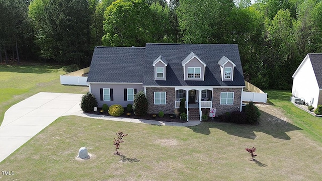 cape cod home with a porch, concrete driveway, stone siding, and a front lawn