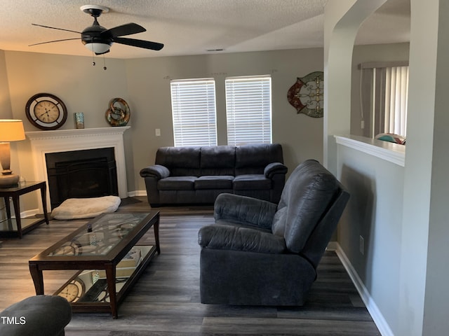 living room featuring baseboards, a ceiling fan, wood finished floors, a textured ceiling, and a fireplace