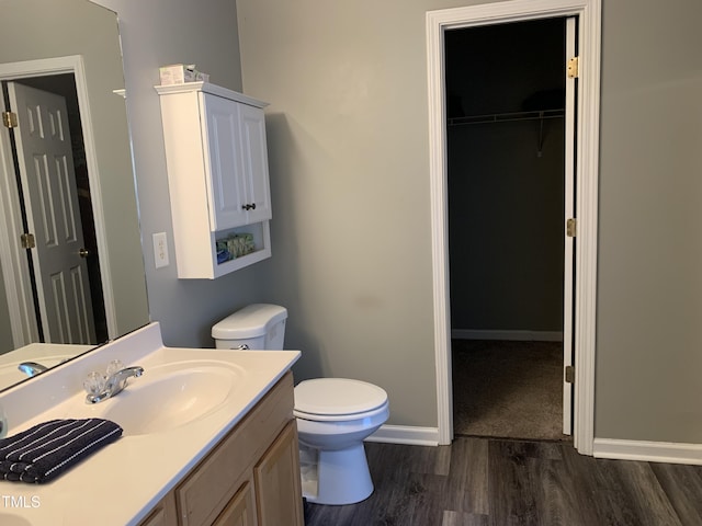 bathroom with baseboards, toilet, wood finished floors, a spacious closet, and vanity