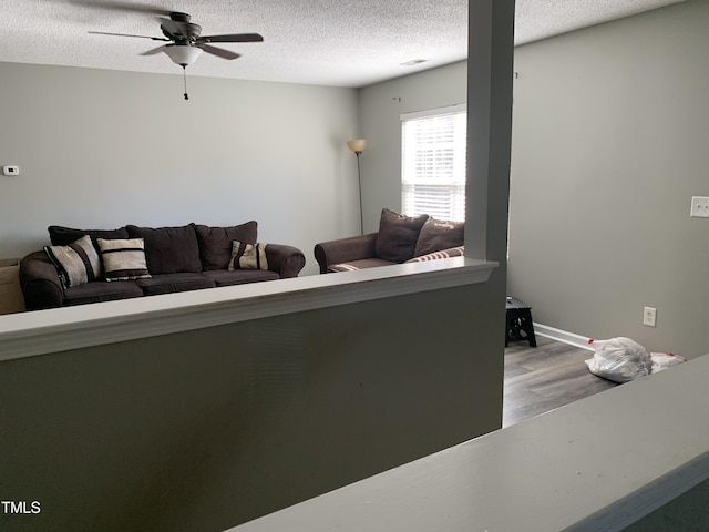 living room featuring a textured ceiling, wood finished floors, visible vents, a ceiling fan, and baseboards