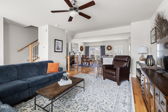 living room featuring a ceiling fan, stairs, and light wood finished floors