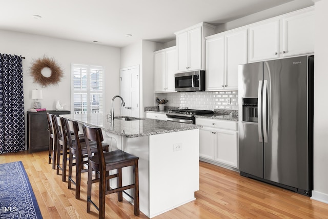 kitchen featuring light wood-type flooring, stainless steel appliances, an island with sink, and a sink