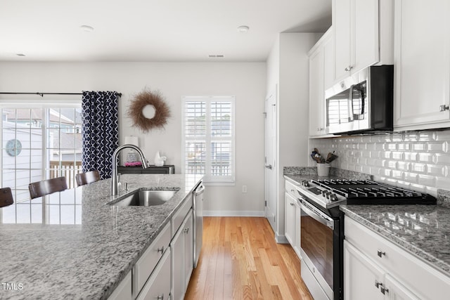 kitchen with backsplash, light wood-type flooring, stainless steel appliances, white cabinetry, and a sink