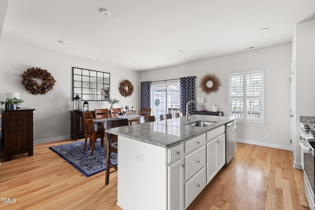 kitchen with white cabinetry, an island with sink, a sink, light wood-style floors, and dishwasher