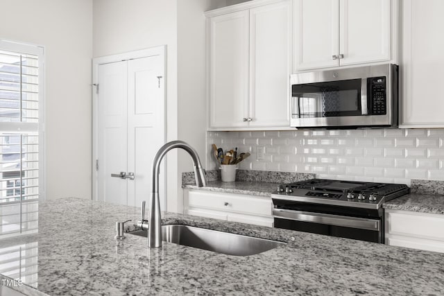 kitchen with tasteful backsplash, light stone countertops, appliances with stainless steel finishes, white cabinetry, and a sink