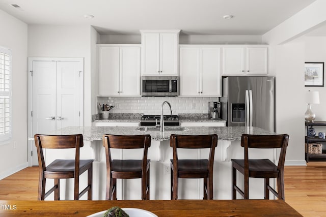 kitchen with a kitchen island with sink, backsplash, white cabinetry, stainless steel appliances, and light wood finished floors