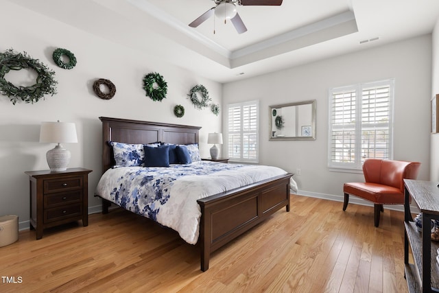 bedroom featuring light wood-type flooring, visible vents, ornamental molding, baseboards, and a raised ceiling