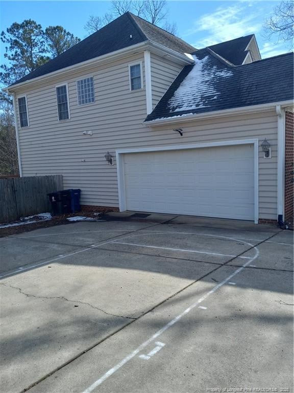 view of side of home featuring roof with shingles, driveway, and fence