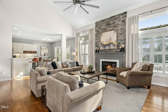 living room with high vaulted ceiling, baseboards, wood finished floors, and a stone fireplace