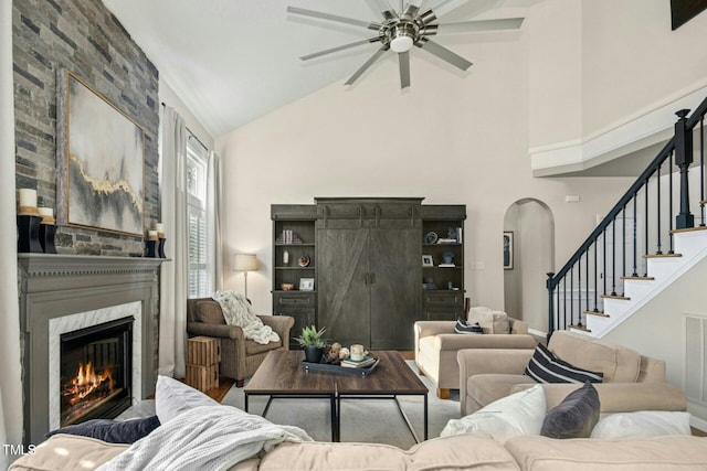 living area featuring arched walkways, ceiling fan, a premium fireplace, stairway, and high vaulted ceiling