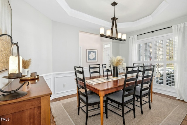 dining area with wainscoting, a raised ceiling, light wood-style flooring, and a notable chandelier