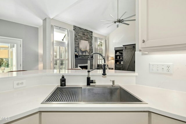 kitchen with a large fireplace, light countertops, a sink, and white cabinetry