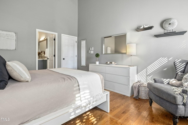 bedroom featuring light wood-style floors, ensuite bath, and a high ceiling