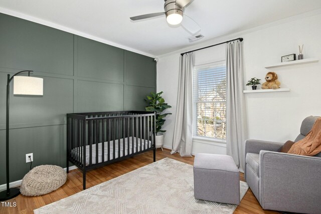 bedroom featuring a nursery area, visible vents, a decorative wall, and wood finished floors