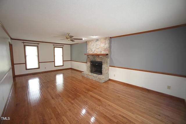 unfurnished living room featuring crown molding, baseboards, wood finished floors, and a stone fireplace