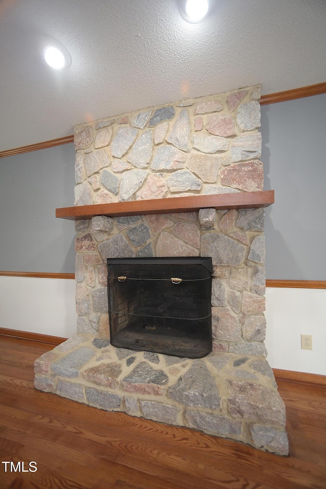 interior details featuring a textured ceiling, ornamental molding, a fireplace, and wood finished floors