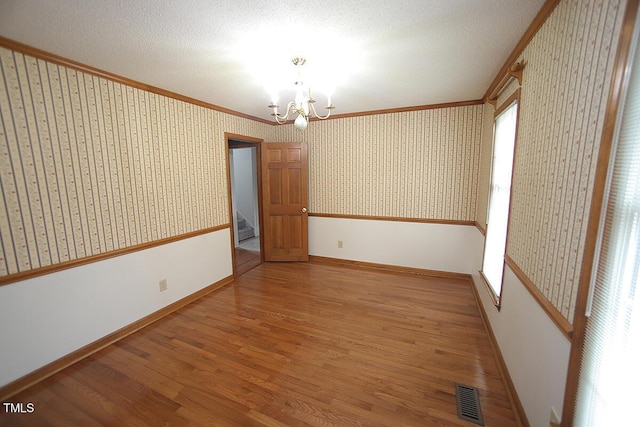 empty room with a notable chandelier, wood finished floors, visible vents, and wallpapered walls