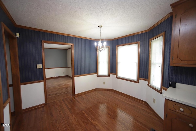 unfurnished dining area featuring a textured ceiling, ornamental molding, dark wood finished floors, and wallpapered walls