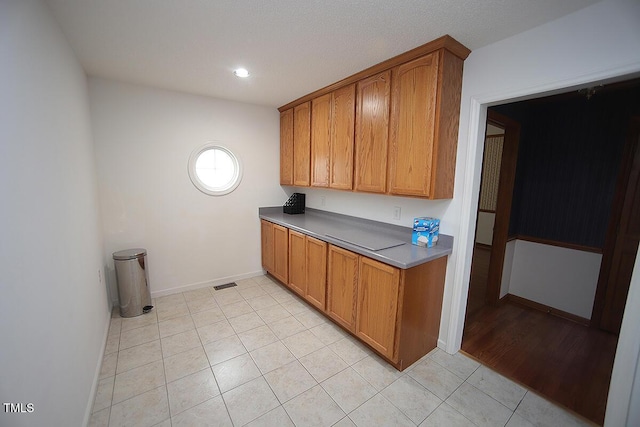 kitchen featuring brown cabinetry, visible vents, baseboards, and light tile patterned floors