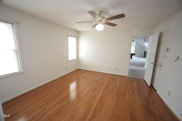 spare room featuring light wood-type flooring, a textured ceiling, baseboards, and a ceiling fan