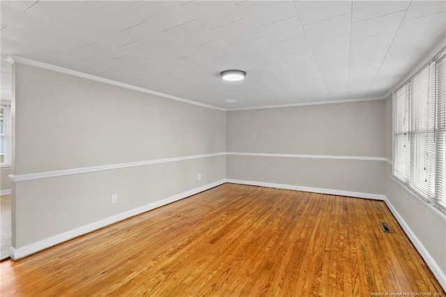 empty room with visible vents, crown molding, baseboards, and wood finished floors