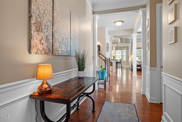 corridor with a wainscoted wall, decorative columns, a decorative wall, ornamental molding, and dark wood-type flooring