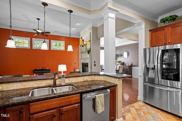 kitchen featuring decorative light fixtures, appliances with stainless steel finishes, a glass covered fireplace, ornamental molding, and a sink