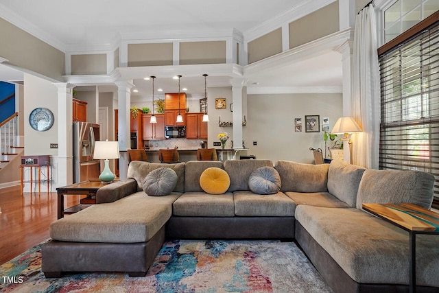 living area with ornate columns, stairway, ornamental molding, and wood finished floors