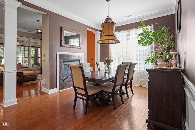 dining room with ornamental molding, wood finished floors, decorative columns, and a premium fireplace