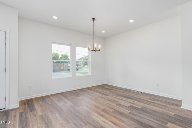 spare room with an inviting chandelier, baseboards, wood finished floors, and recessed lighting