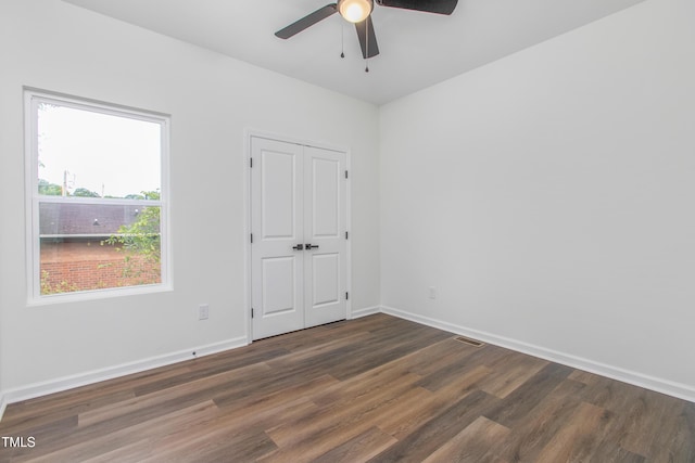 empty room with dark wood-type flooring, visible vents, ceiling fan, and baseboards