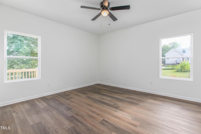 empty room with a healthy amount of sunlight, dark wood-style floors, baseboards, and a ceiling fan