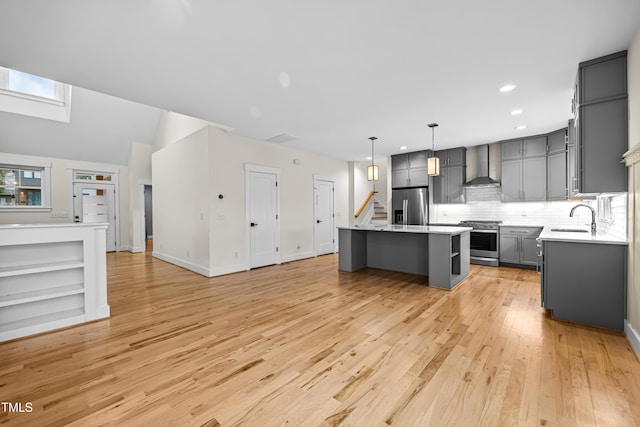 kitchen with wall chimney exhaust hood, appliances with stainless steel finishes, gray cabinets, light countertops, and a sink