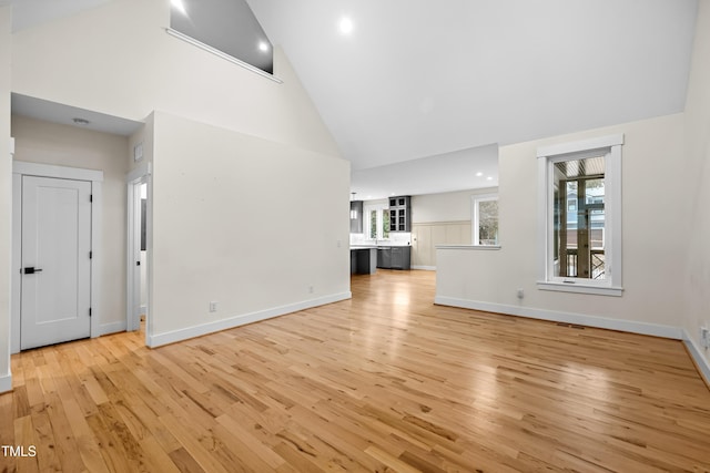 unfurnished living room with high vaulted ceiling, light wood-type flooring, and baseboards