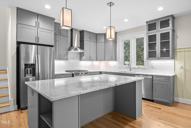 kitchen with wall chimney exhaust hood, a kitchen island, appliances with stainless steel finishes, light stone counters, and gray cabinetry