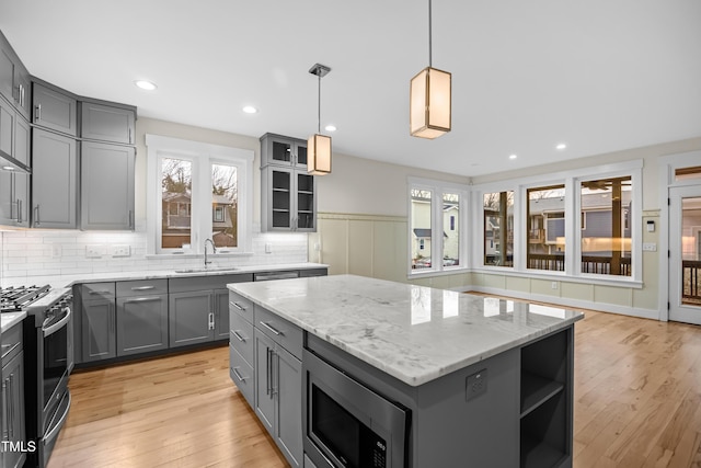 kitchen featuring a kitchen island, appliances with stainless steel finishes, light stone countertops, gray cabinetry, and a sink