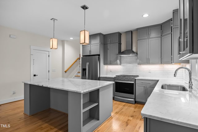 kitchen featuring gray cabinetry, stainless steel appliances, a kitchen island, a sink, and wall chimney range hood