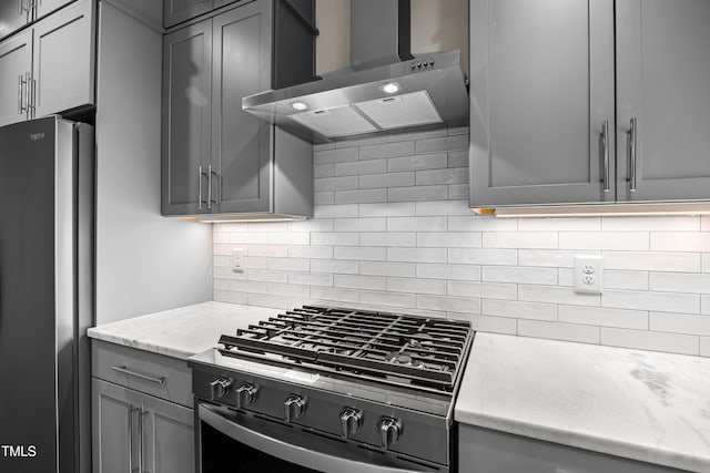 kitchen with decorative backsplash, wall chimney exhaust hood, freestanding refrigerator, gas range oven, and gray cabinets