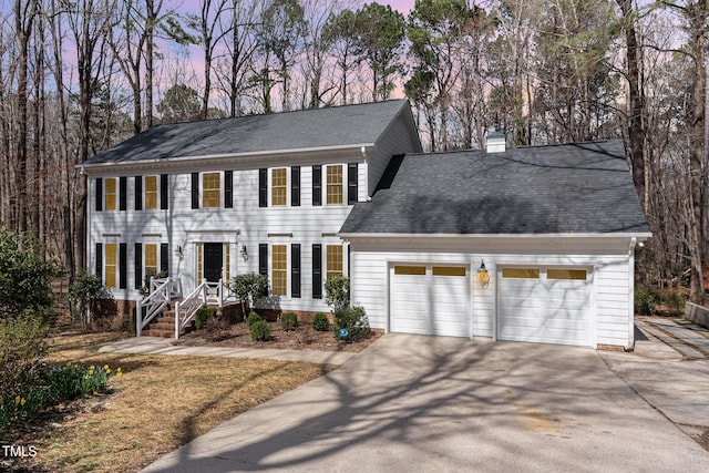 colonial inspired home with an attached garage, a chimney, driveway, and a shingled roof