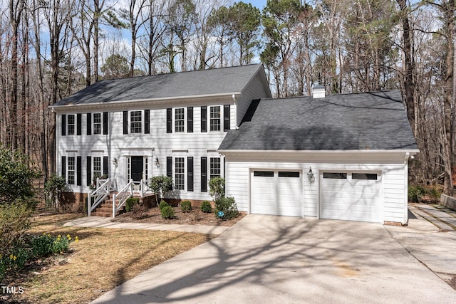 colonial inspired home with roof with shingles, a garage, driveway, and a chimney