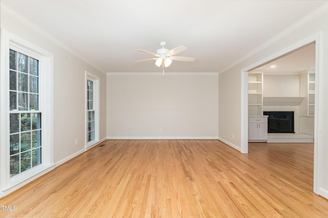 empty room with a glass covered fireplace, light wood-type flooring, baseboards, and ornamental molding