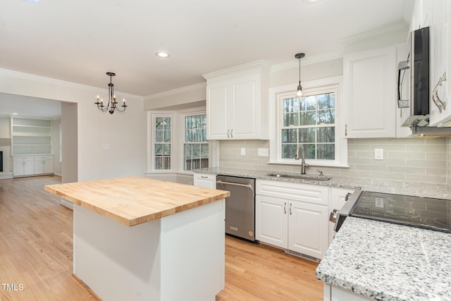 kitchen with light wood-style flooring, ornamental molding, a sink, appliances with stainless steel finishes, and butcher block counters