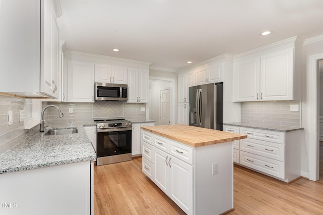 kitchen featuring a kitchen island, butcher block countertops, appliances with stainless steel finishes, white cabinets, and a sink