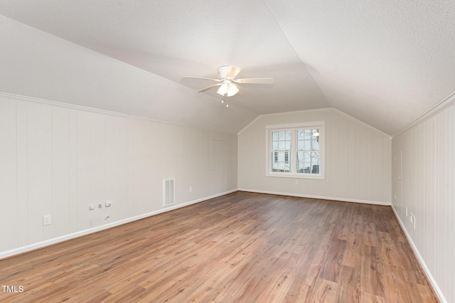 additional living space with visible vents, a textured ceiling, lofted ceiling, and hardwood / wood-style flooring