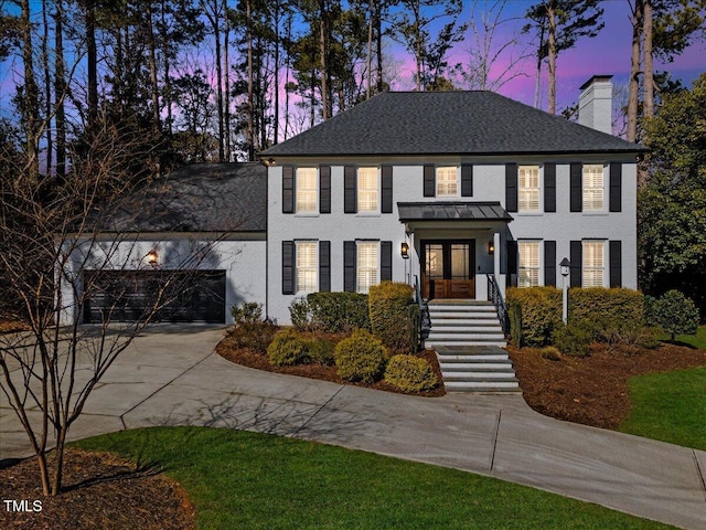 view of front of house with a garage, a chimney, concrete driveway, and french doors