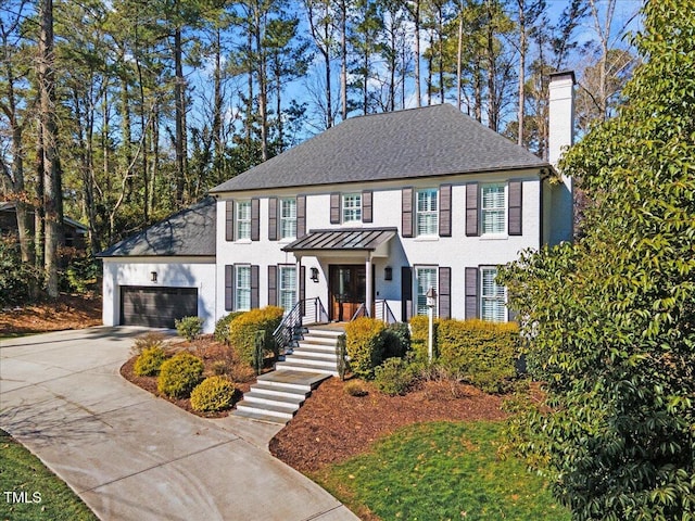 view of front of house featuring concrete driveway, a chimney, metal roof, an attached garage, and a standing seam roof