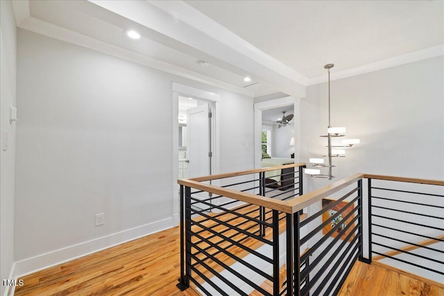 corridor with light wood-style floors, crown molding, and an upstairs landing